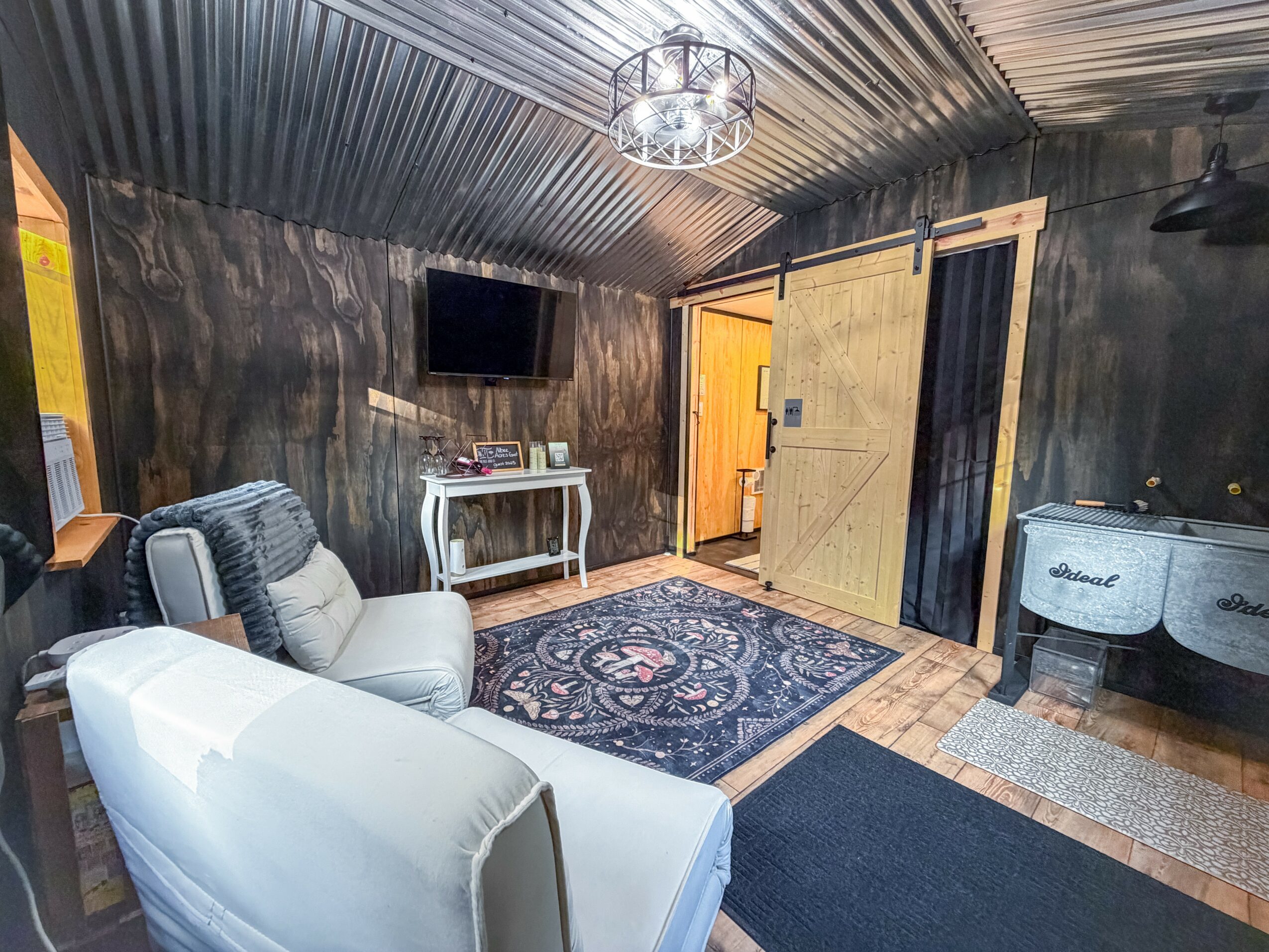 Room with black walls and ceiling, white furniture, a TV, a rug, and a sliding barn door, with a doorway leading outside.