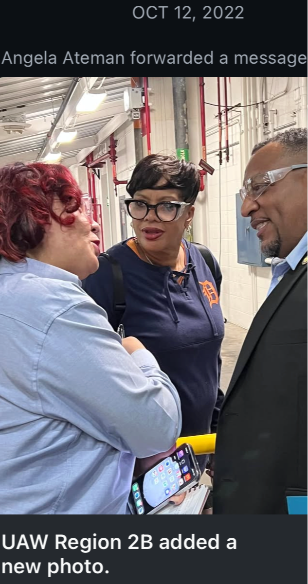 Three people engaged in conversation in an industrial setting, with one holding a smartphone and a yellow object.