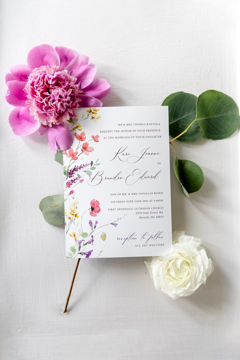 Invitation card with floral design, surrounded by pink and white flowers and green leaves, on a white background.