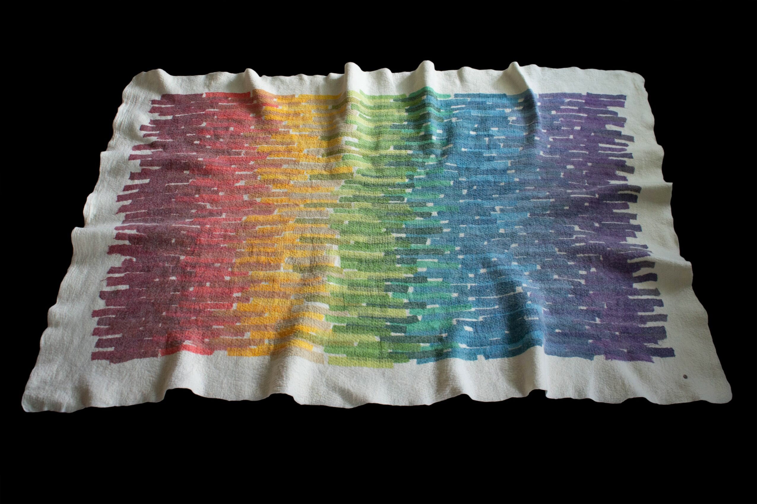 Colorful fabric with rainbow stripes, wrinkled, on a black background.