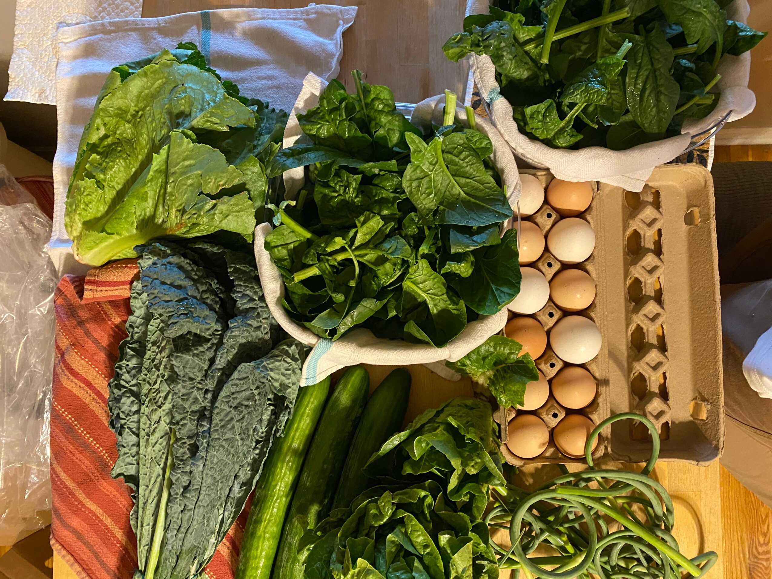 Fresh green vegetables, eggs in a carton, and cucumbers on a wooden table.