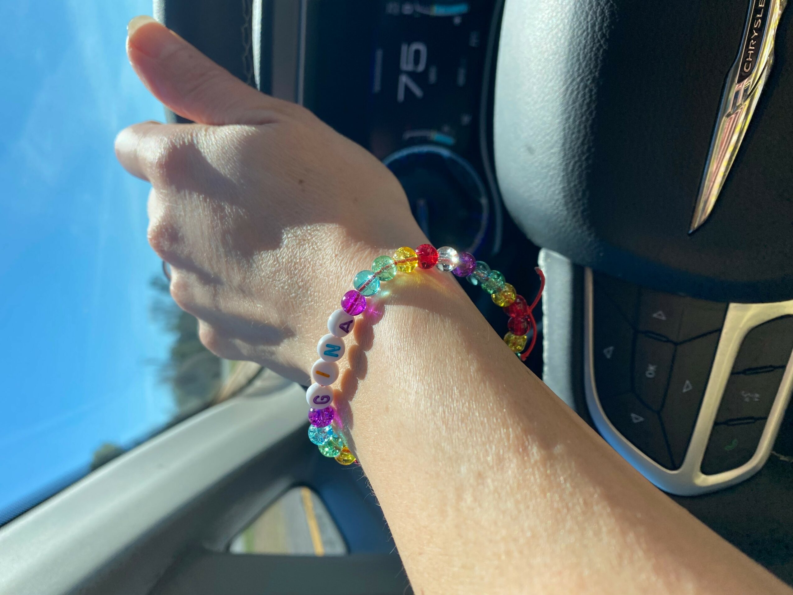 Person's arm with colorful beaded bracelet inside a car, view of the sky through the window