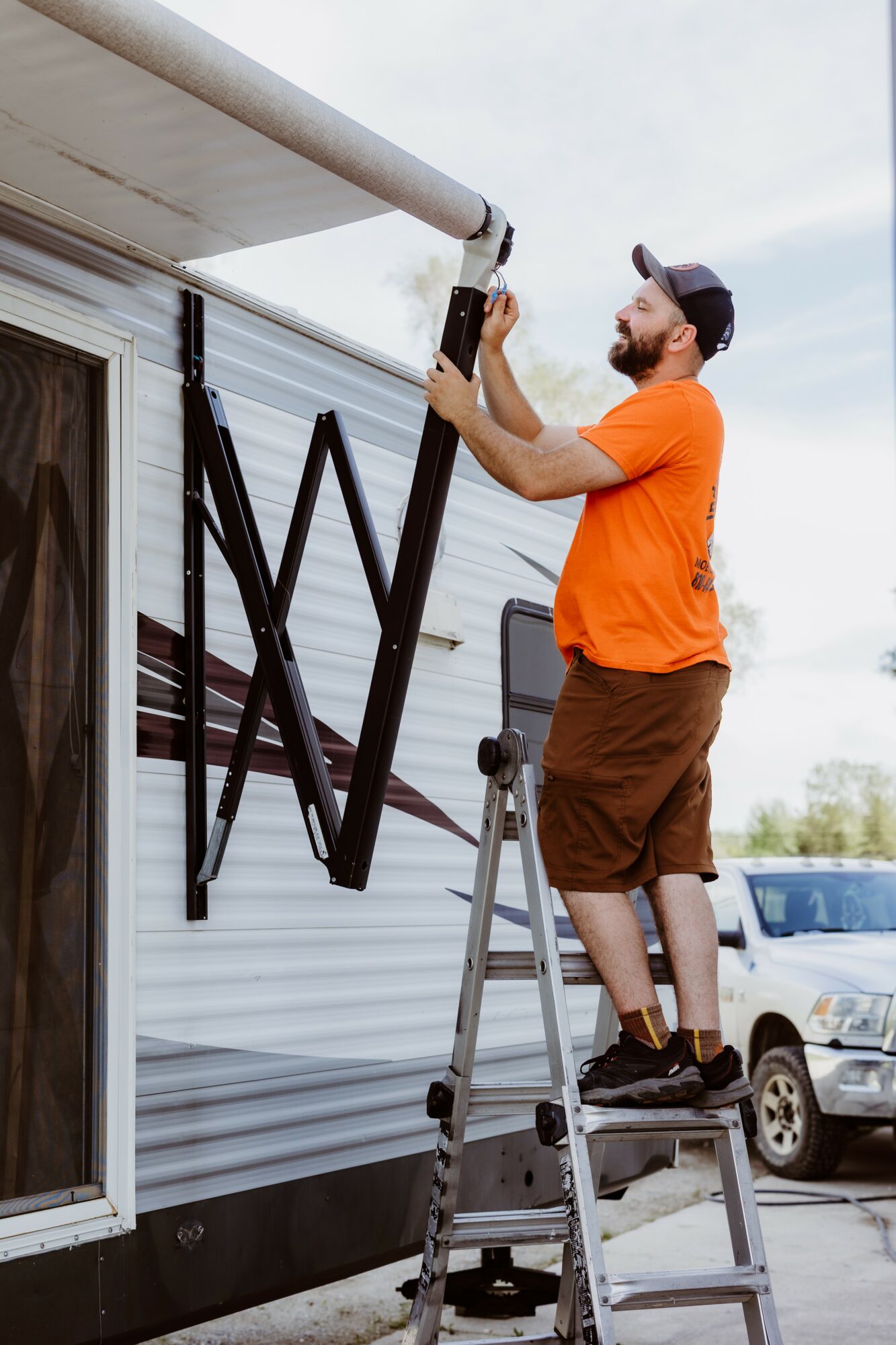Man on ladder installing a large black letter on a building exterior, wearing an orange shirt and brown shorts.