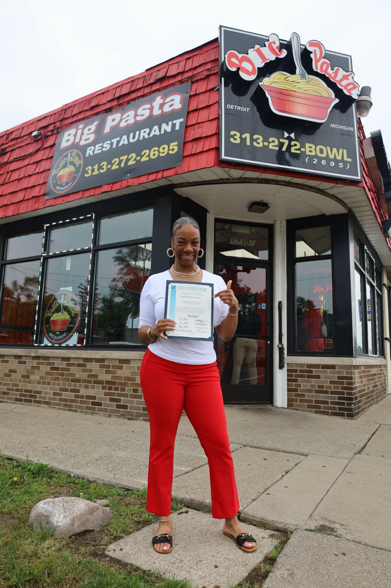 Woman in red pants holding a document outside a restaurant with a sign advertising cake, cupcake, and ice cream.