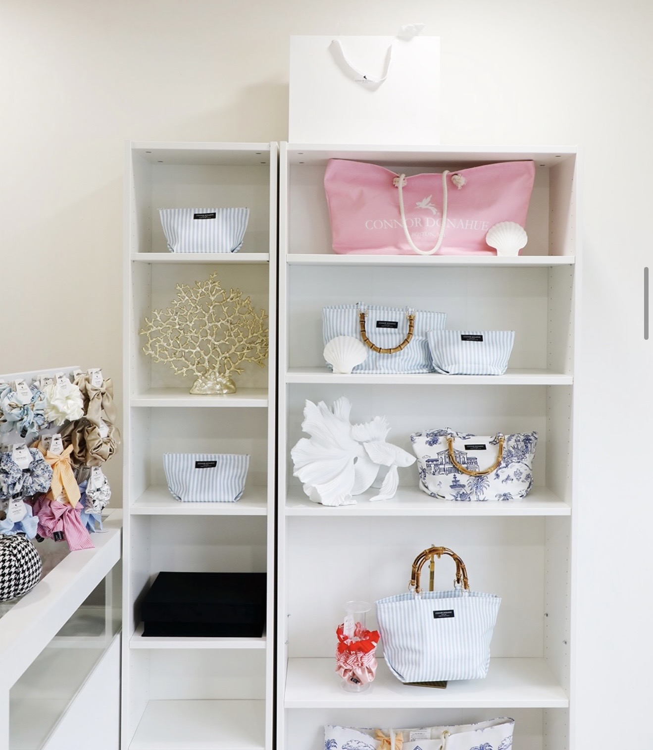 White shelving unit with baskets, decorative items, and a pink bag on top, against a light-colored wall.