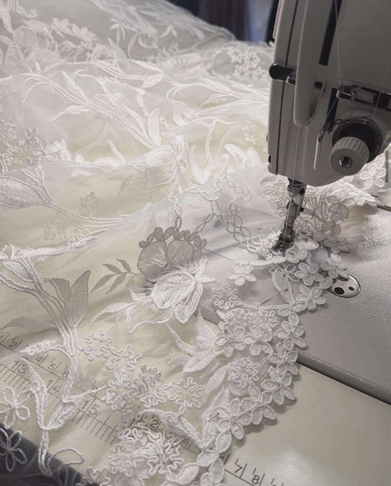 A sewing machine stitches intricate lace onto fabric, creating detailed floral patterns on a bedspread.