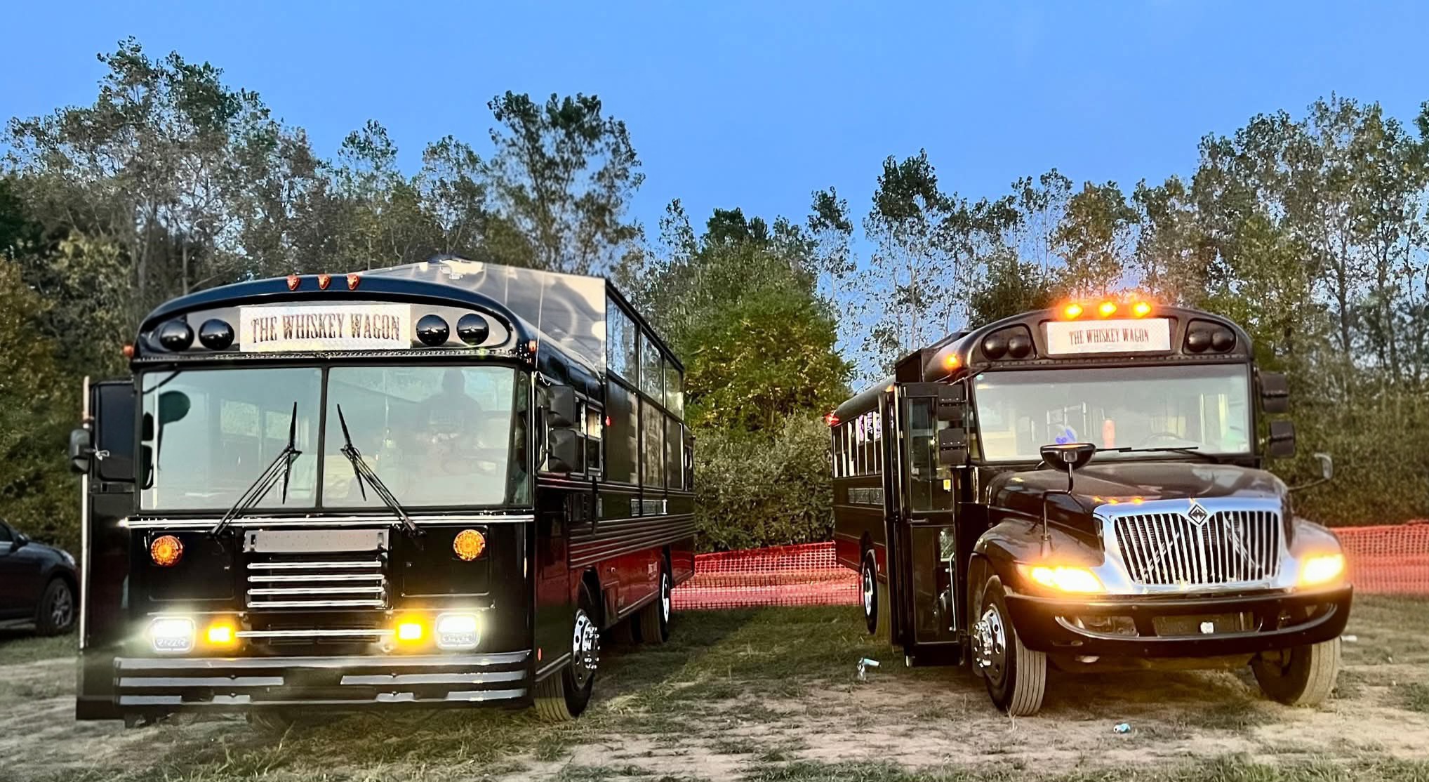 Two buses parked outdoors with trees and a blue sky in the background.