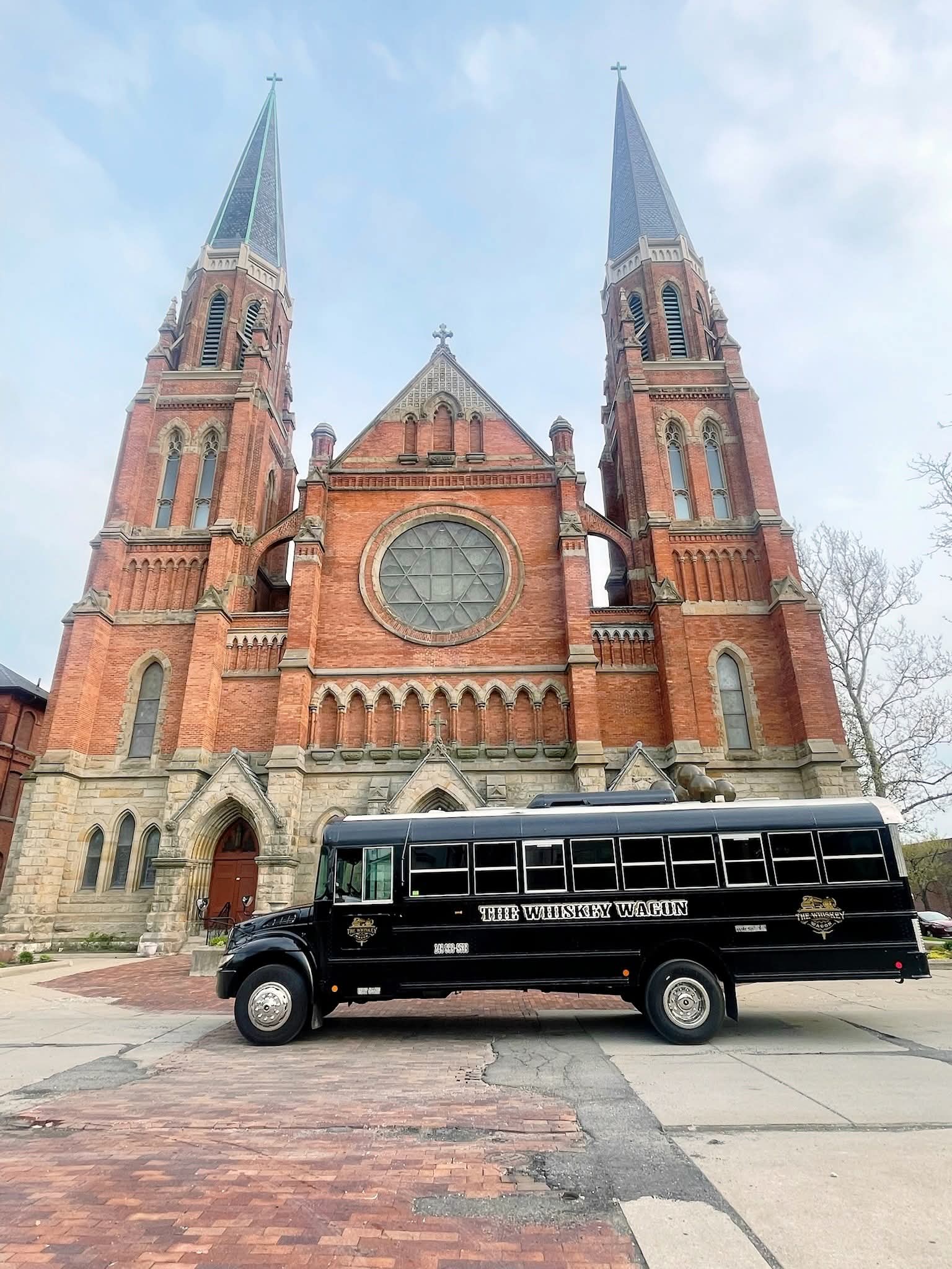 Front view of a large brick church with two tall steeples and a black vehicle parked in front.