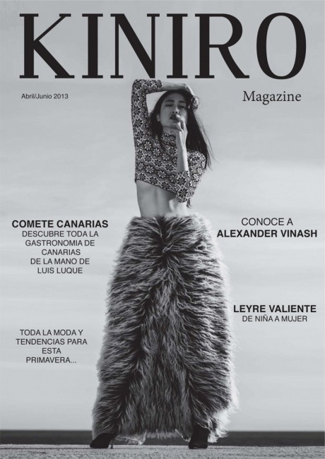 Black and white magazine cover featuring a woman with long hair, wearing a furry skirt and patterned top, standing with hand on face.