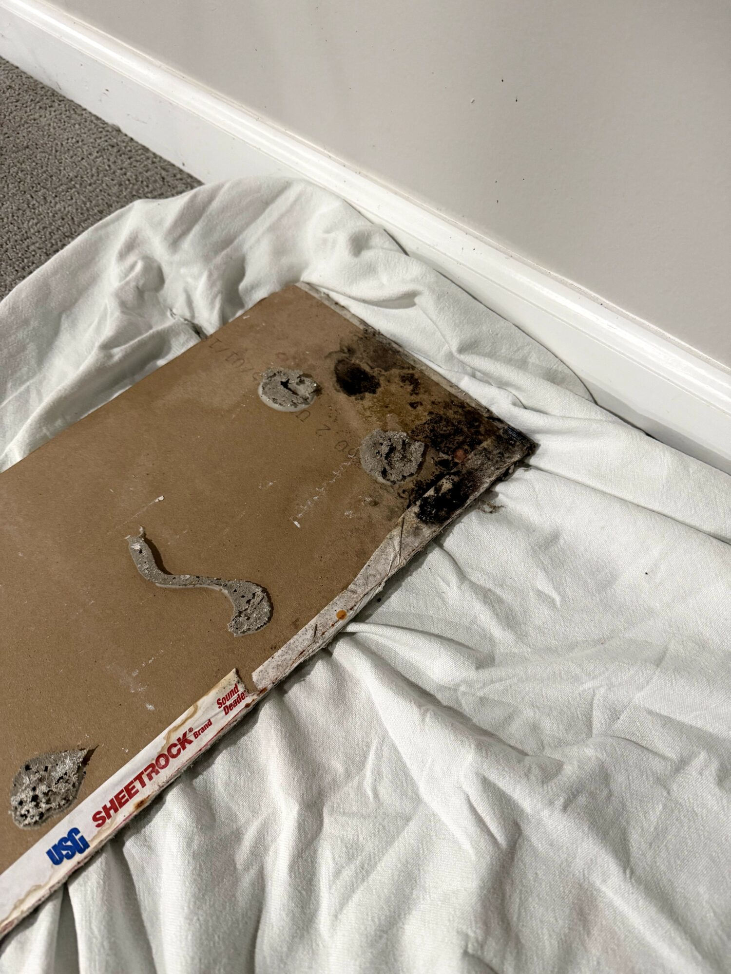 Burned and damaged cardboard box on white fabric, with a white wall and baseboard in the background.