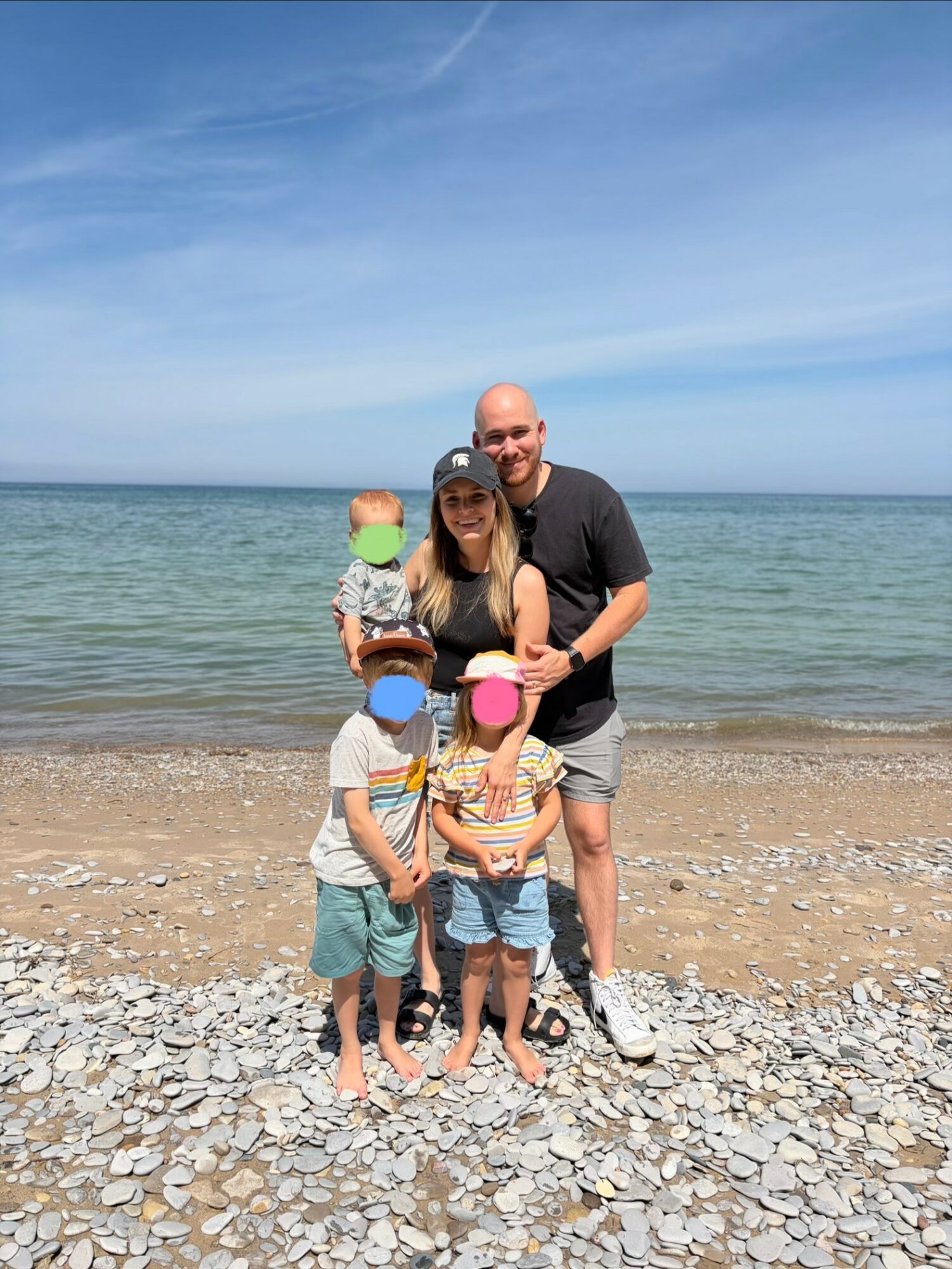 Family of four standing on a rocky beach with the ocean and sky in the background, smiling at the camera.