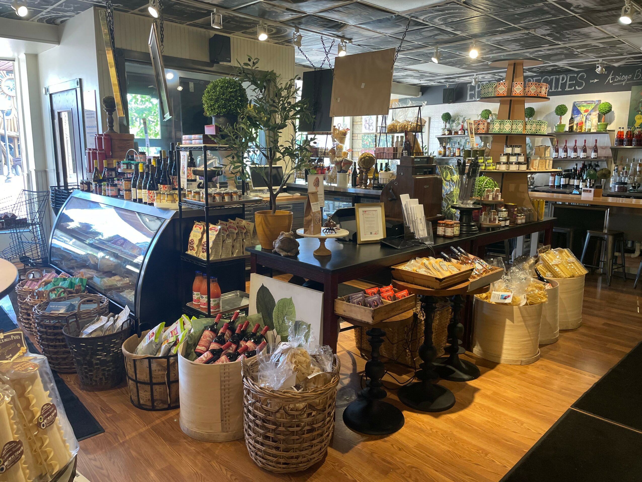 Interior of a store with shelves, baskets, and a counter displaying various products, with a TV and plants visible.