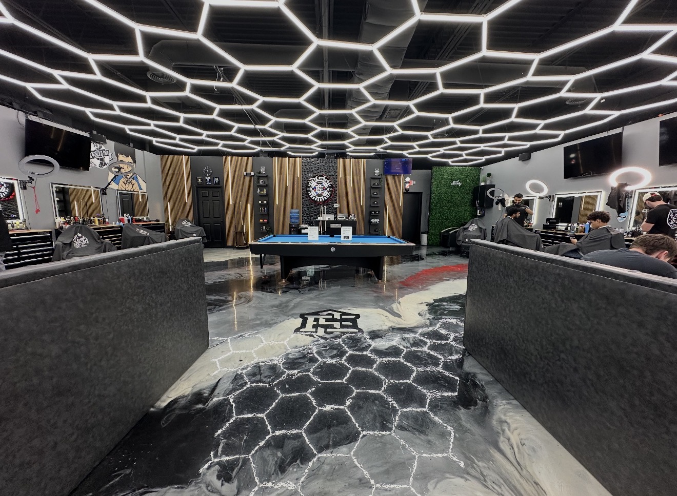 Indoor gaming area with a ping pong table, hexagonal ceiling lights, and people playing games.