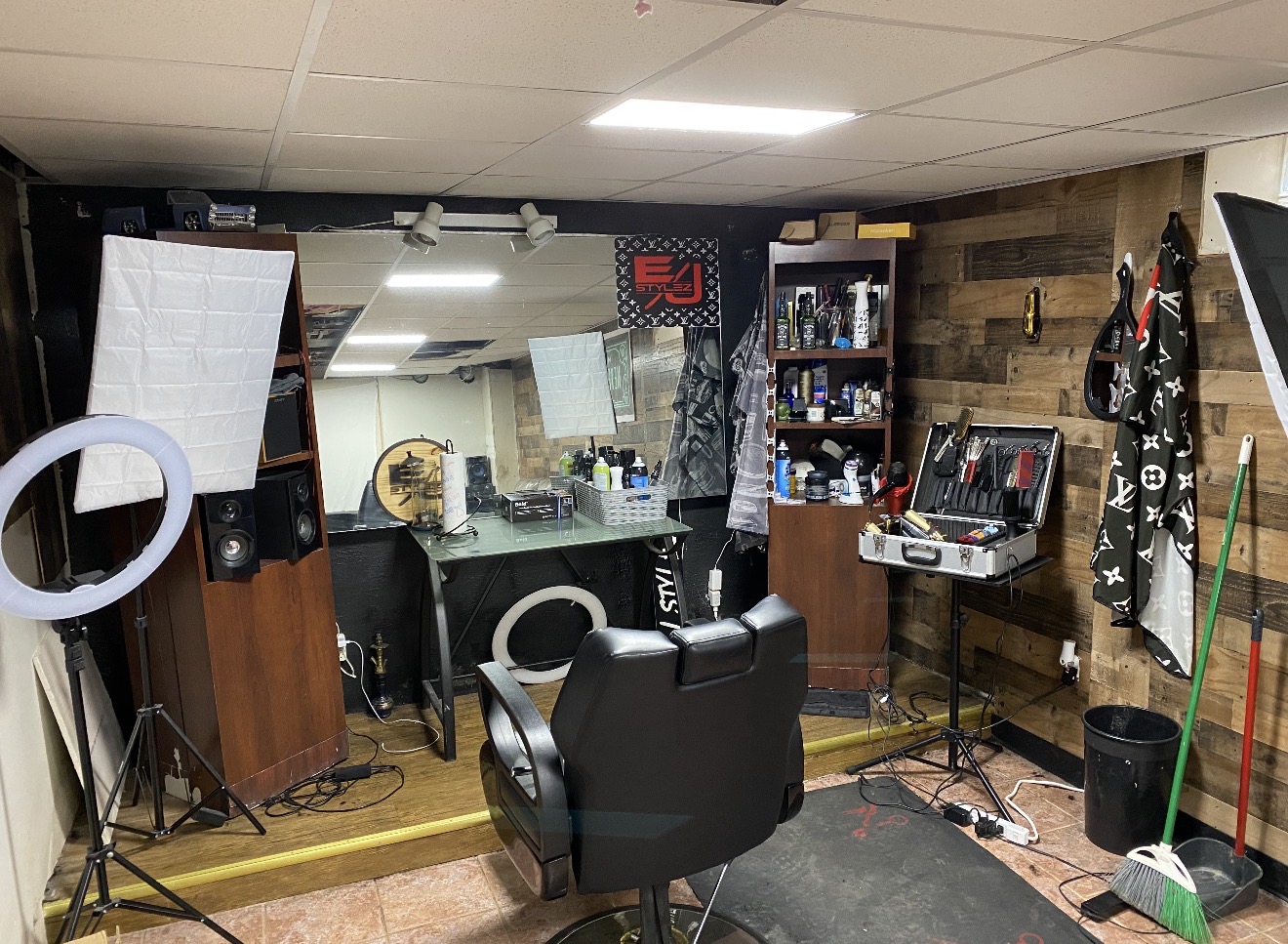 Barber shop with chair, shelves, and equipment, mirror, and cleaning tools in a small room.