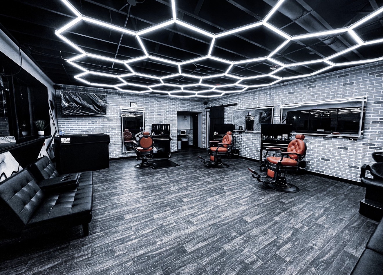 Modern salon with illuminated hexagonal ceiling lights, chairs, and mirrors, featuring dark flooring and white brick walls.