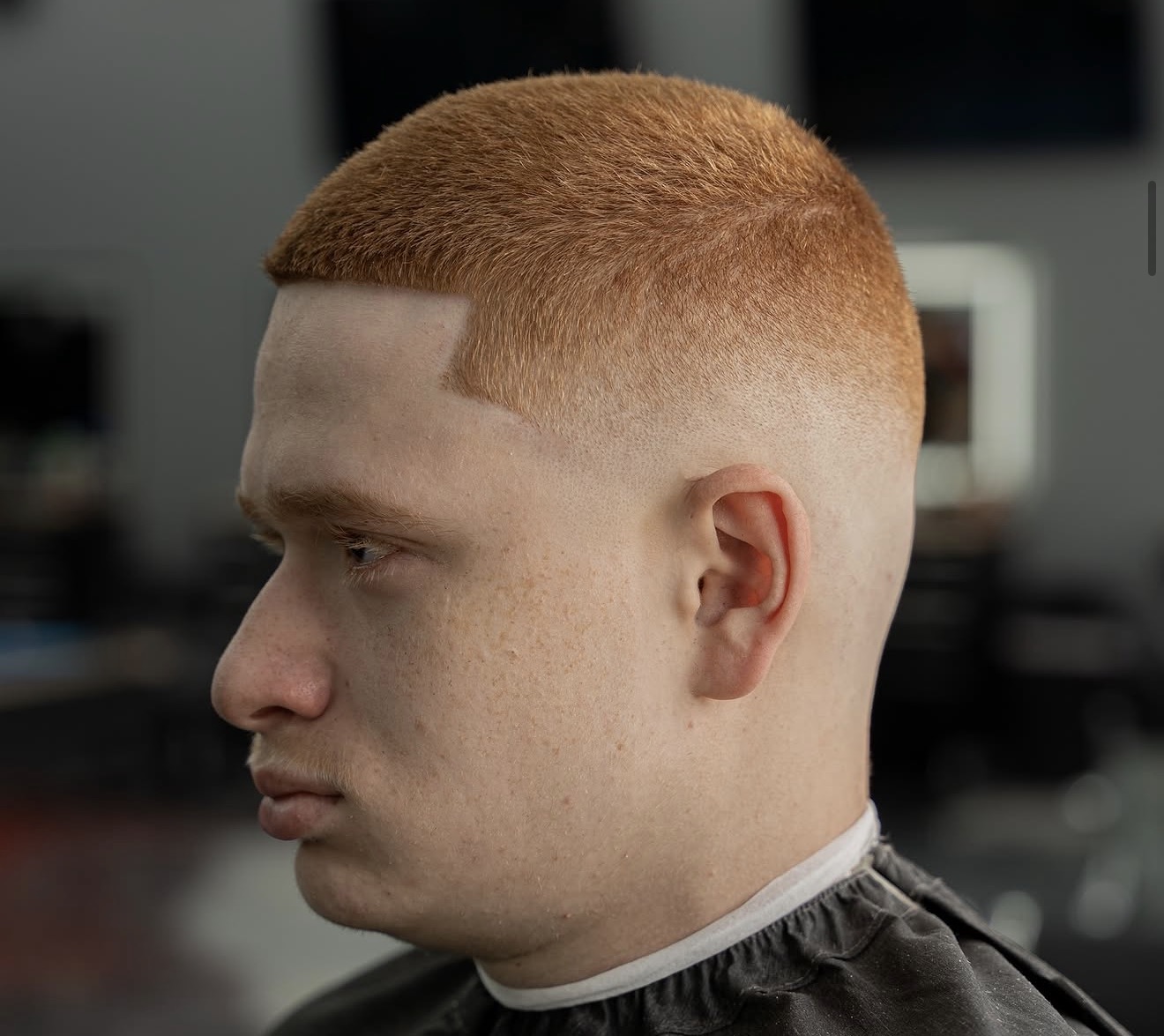 Side profile of a young man with short, reddish hair in a barbershop chair, background blurred.