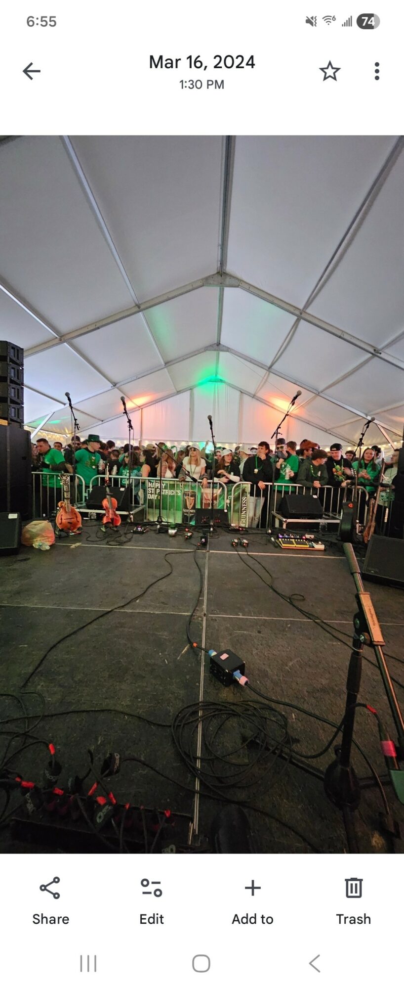 Group of people performing on stage under a large tent with lighting and equipment, audience in front, evening setting.