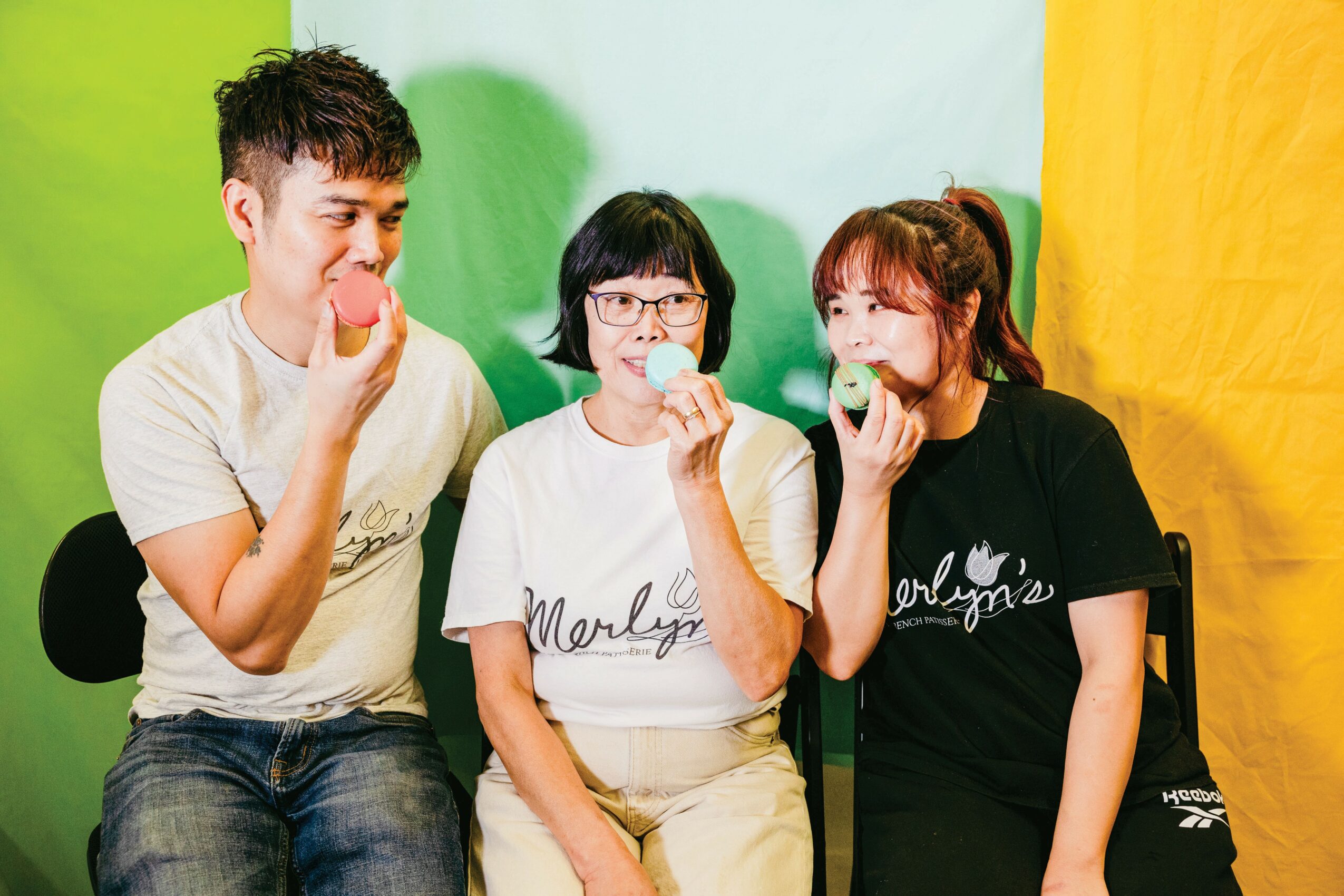 Three young women sitting together, smiling and eating snacks, with colorful background walls.