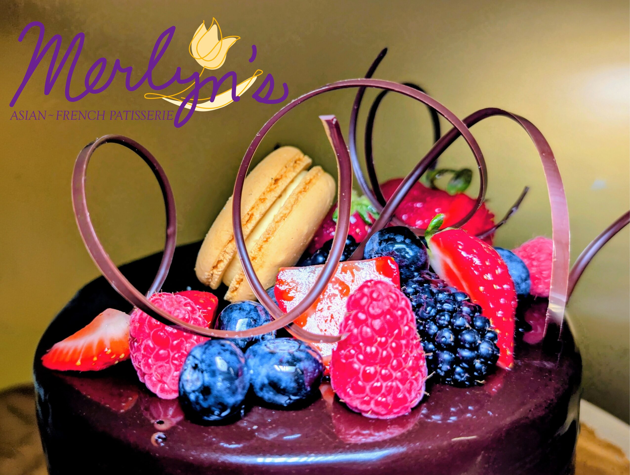 Chocolate cake decorated with strawberries, raspberries, blueberries, and a macaron, with decorative chocolate hearts on top.