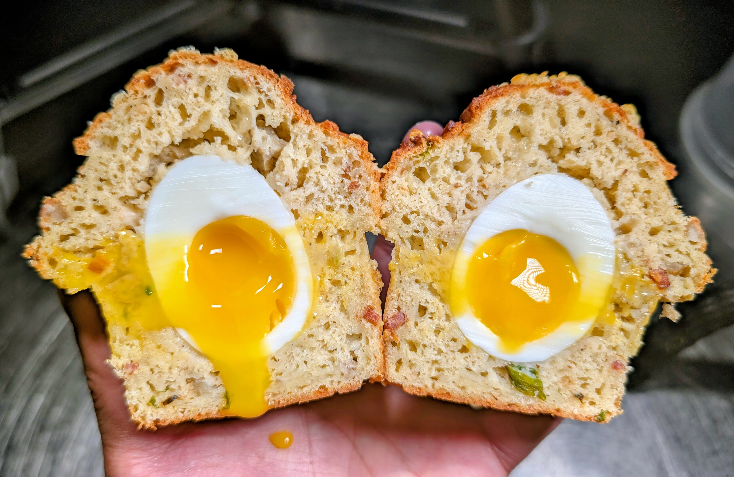 Two halves of a baked good with a soft, fluffy interior and a runny egg yolk in the center, held in a hand.