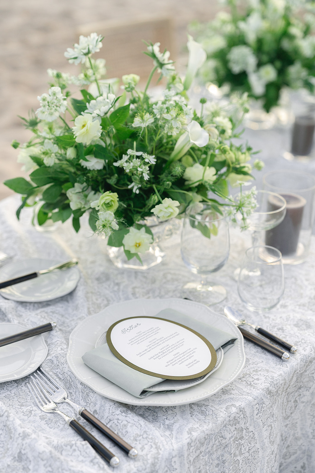 Elegant table setting with a large white floral centerpiece, plates, glasses, and cutlery on a textured tablecloth.