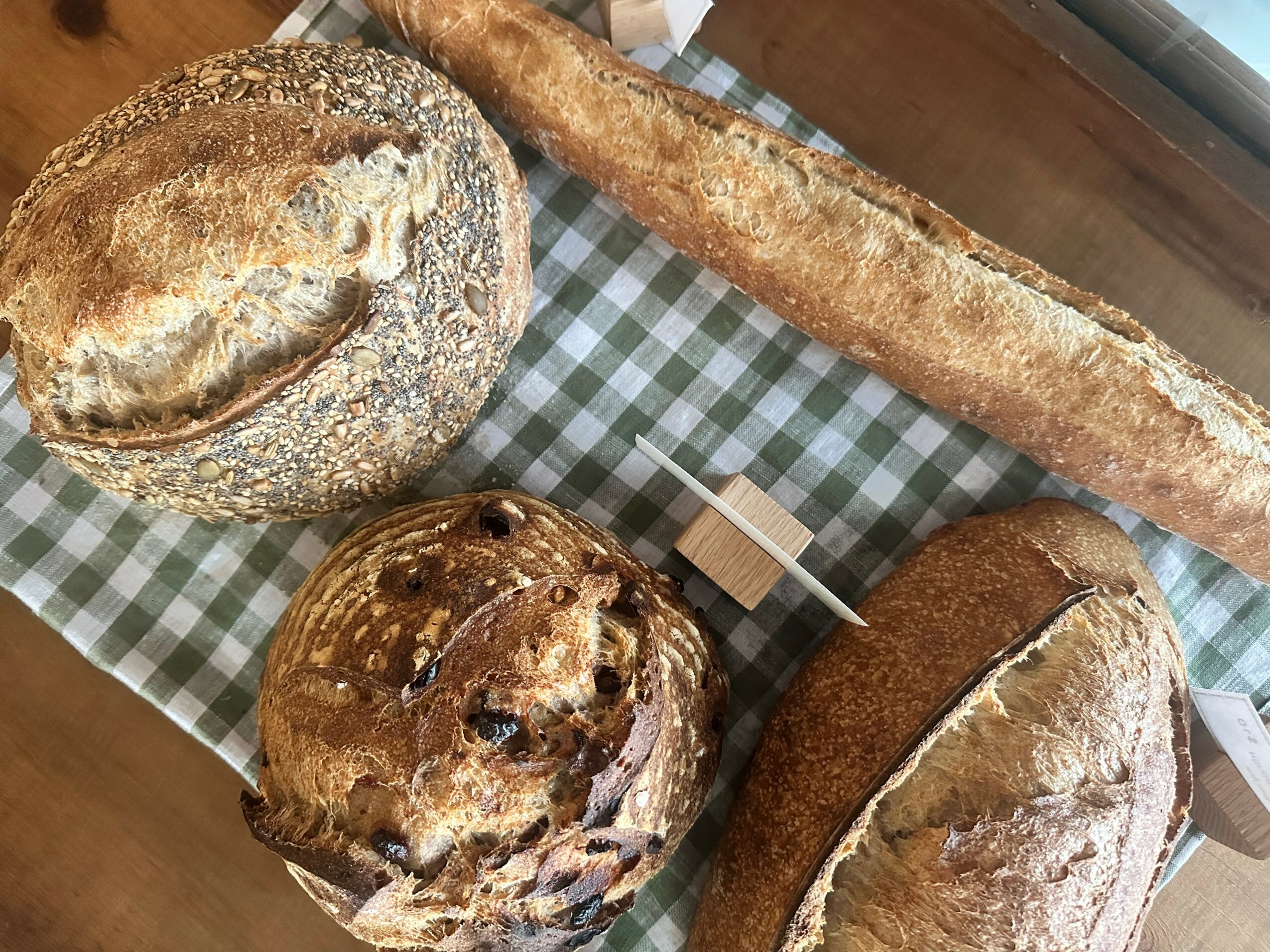 Three different types of bread on a checkered cloth, with a long baguette, round loaf, and a large, round, crusty bread.
