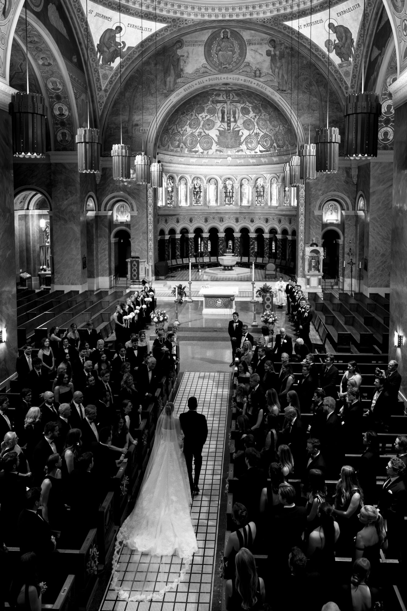 A wedding ceremony inside a grand church with a bride and groom walking down the aisle, surrounded by seated guests.