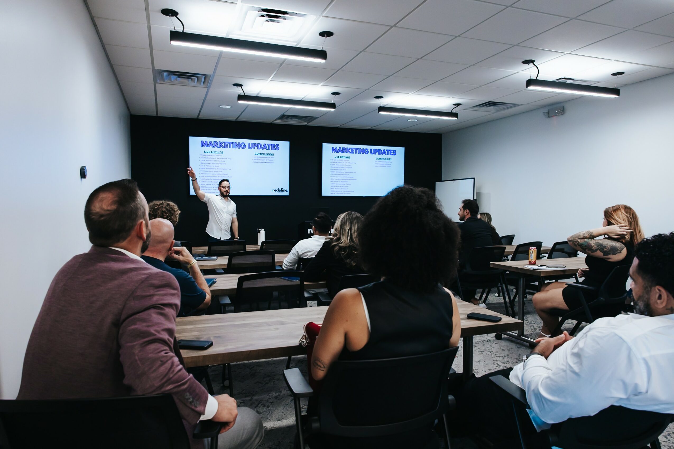 People attending a presentation in a conference room with two screens displaying a slide titled 'Manufacturing Update'.