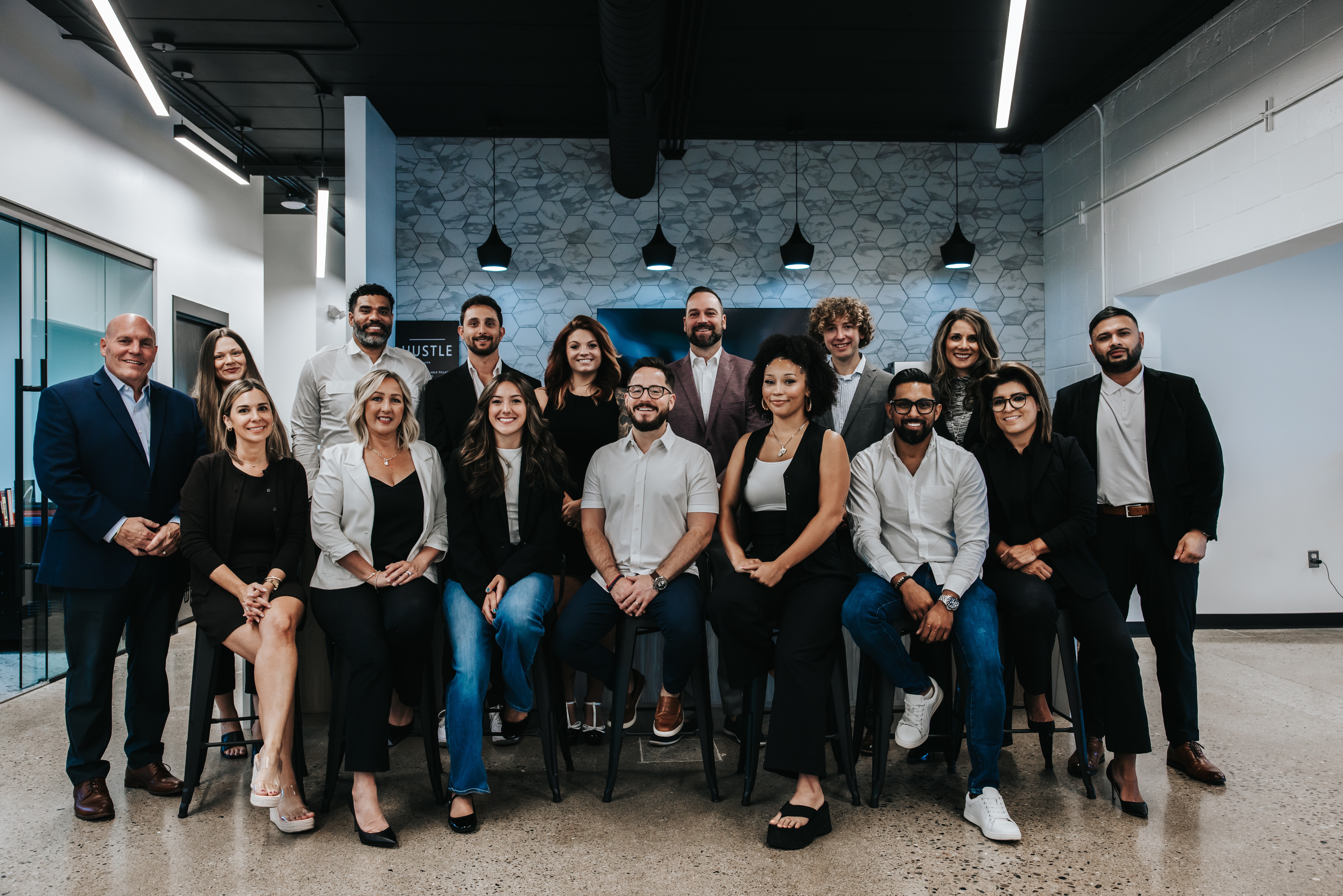 Group of 16 diverse professionals in a modern office, posing for a photo, some seated and some standing, smiling.