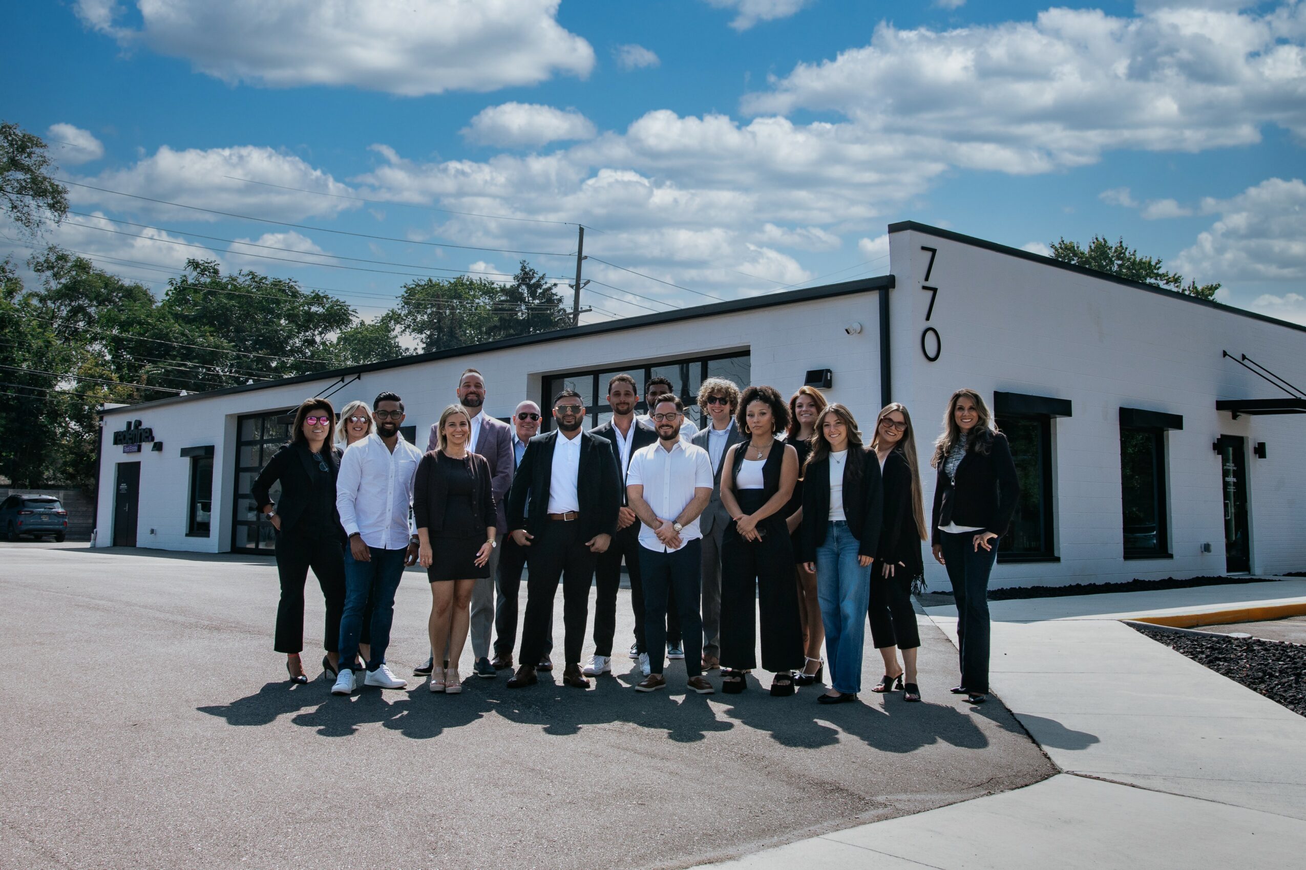 Group of people standing outside a white building with black accents under a partly cloudy sky.
