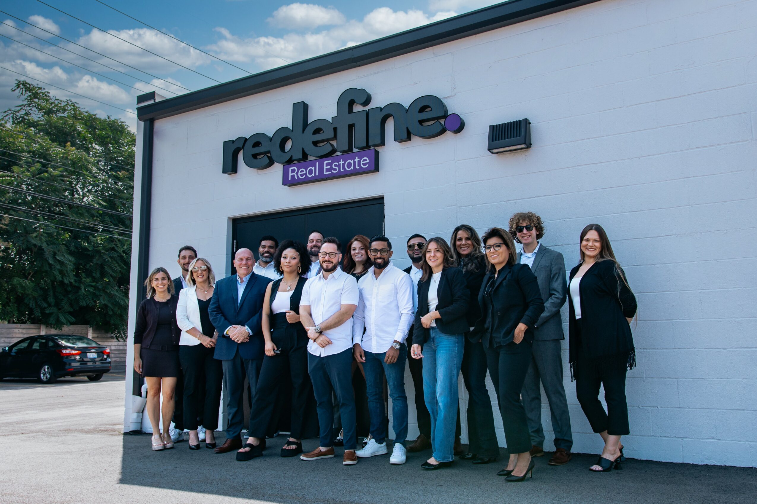 Group of people standing outside a building with a sign that reads 'redefine Real Estate'.