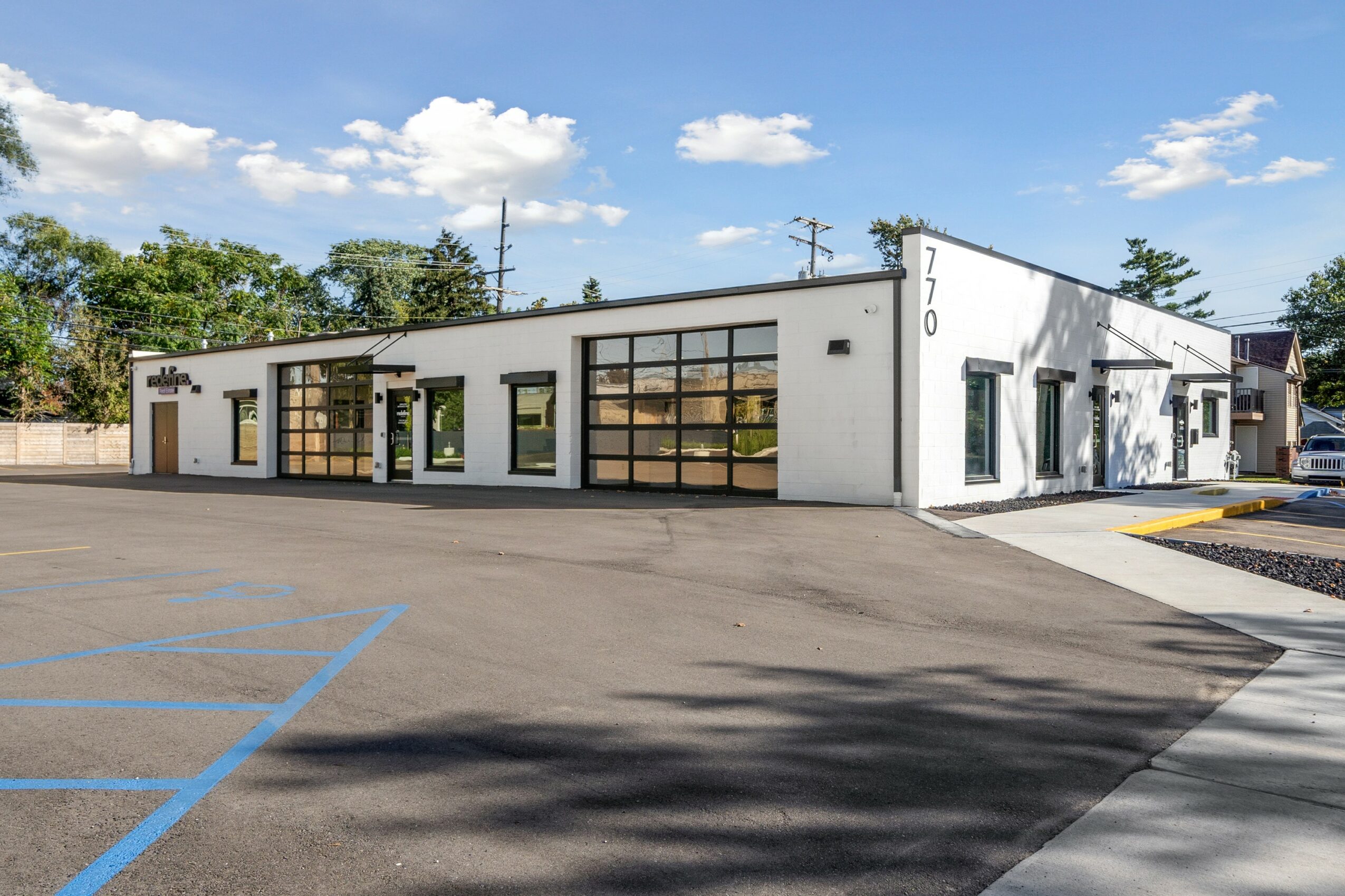 Single-story commercial building with large windows, white exterior, and parking lot in front, under a partly cloudy sky.