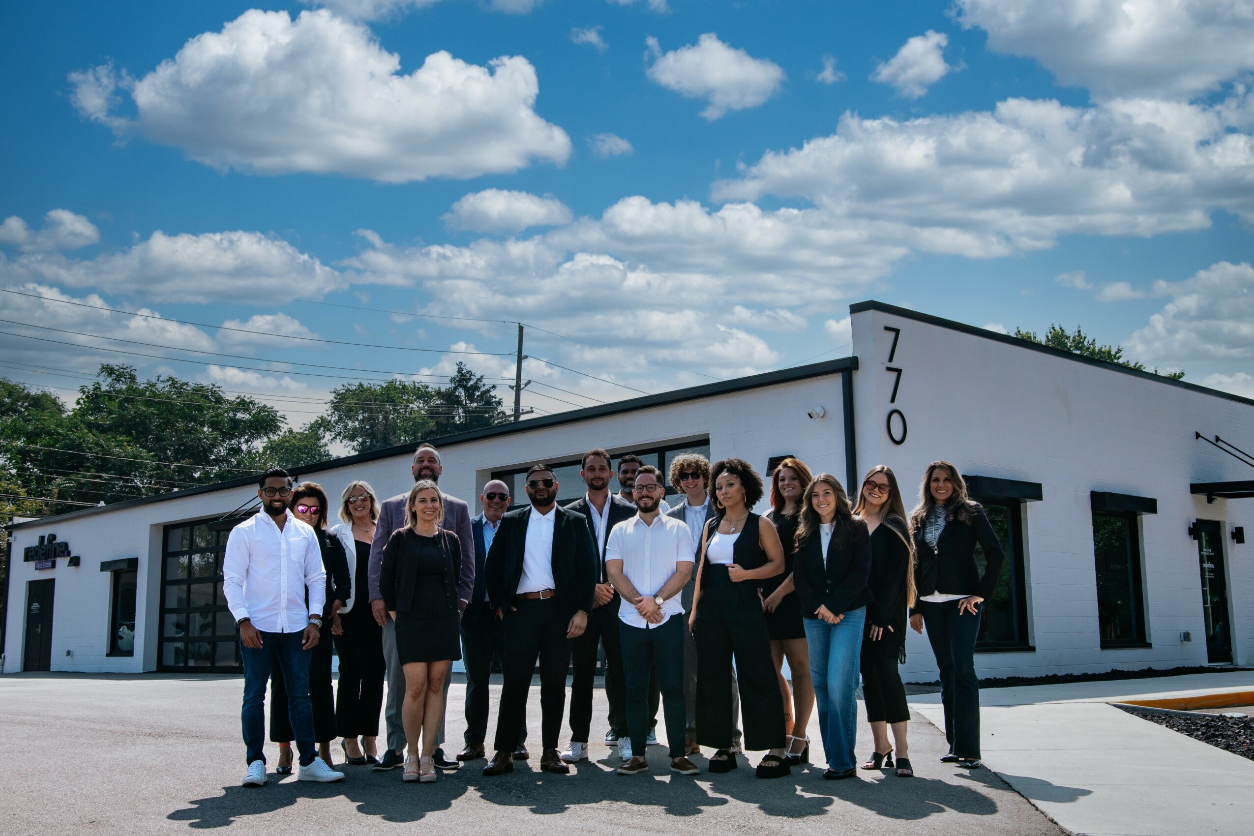 Group of people standing outside a modern white building with the number 770 on it, under a partly cloudy sky.