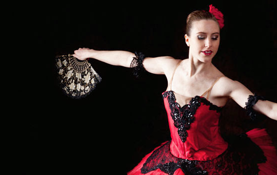 A woman in a red and black dress with lace details, holding a lace fan, against a black background.