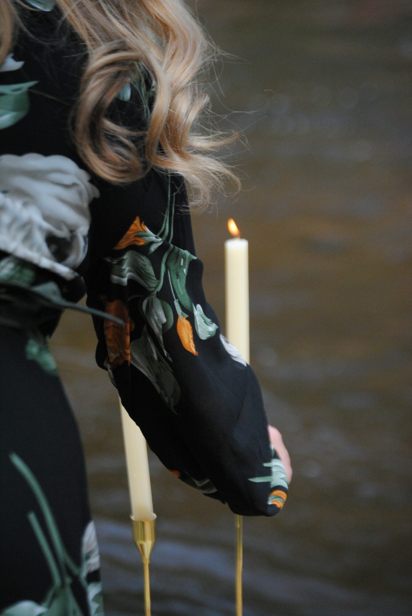 Person holding a black bag with a floral pattern, near a lit candle, with water in the background.