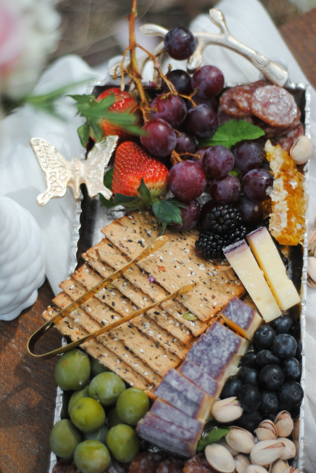 Assorted fruits, crackers, cheese, and a decorative butterfly on a platter.