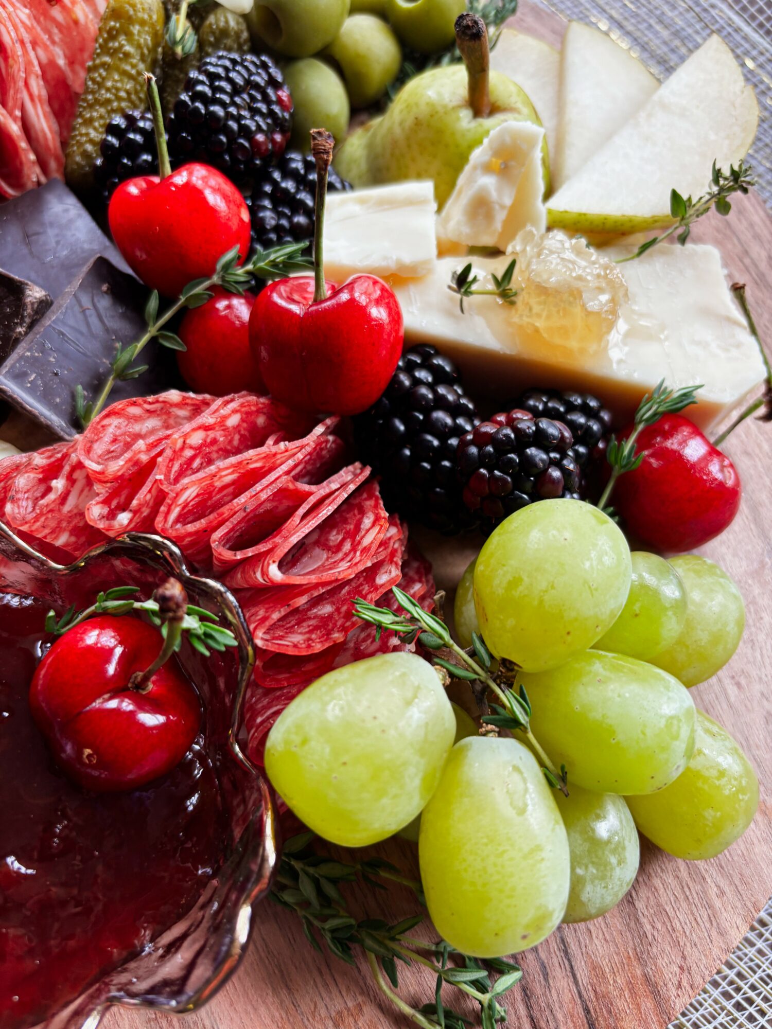Assorted fruits and cheese, including grapes, cherries, blackberries, and sliced pears, arranged on a wooden surface.