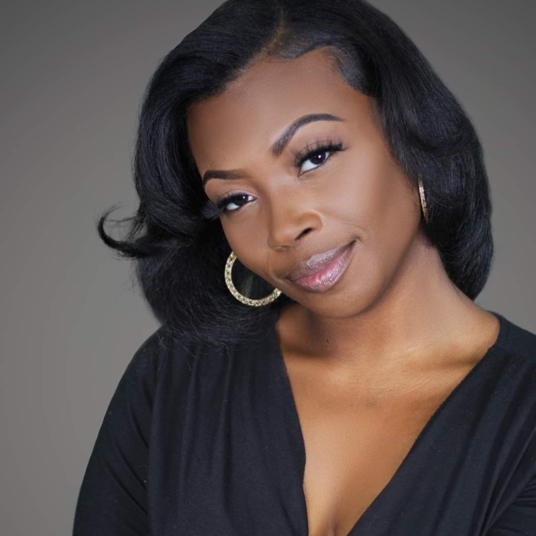 Portrait of a woman with shoulder-length black hair, wearing hoop earrings and a black top, smiling softly.