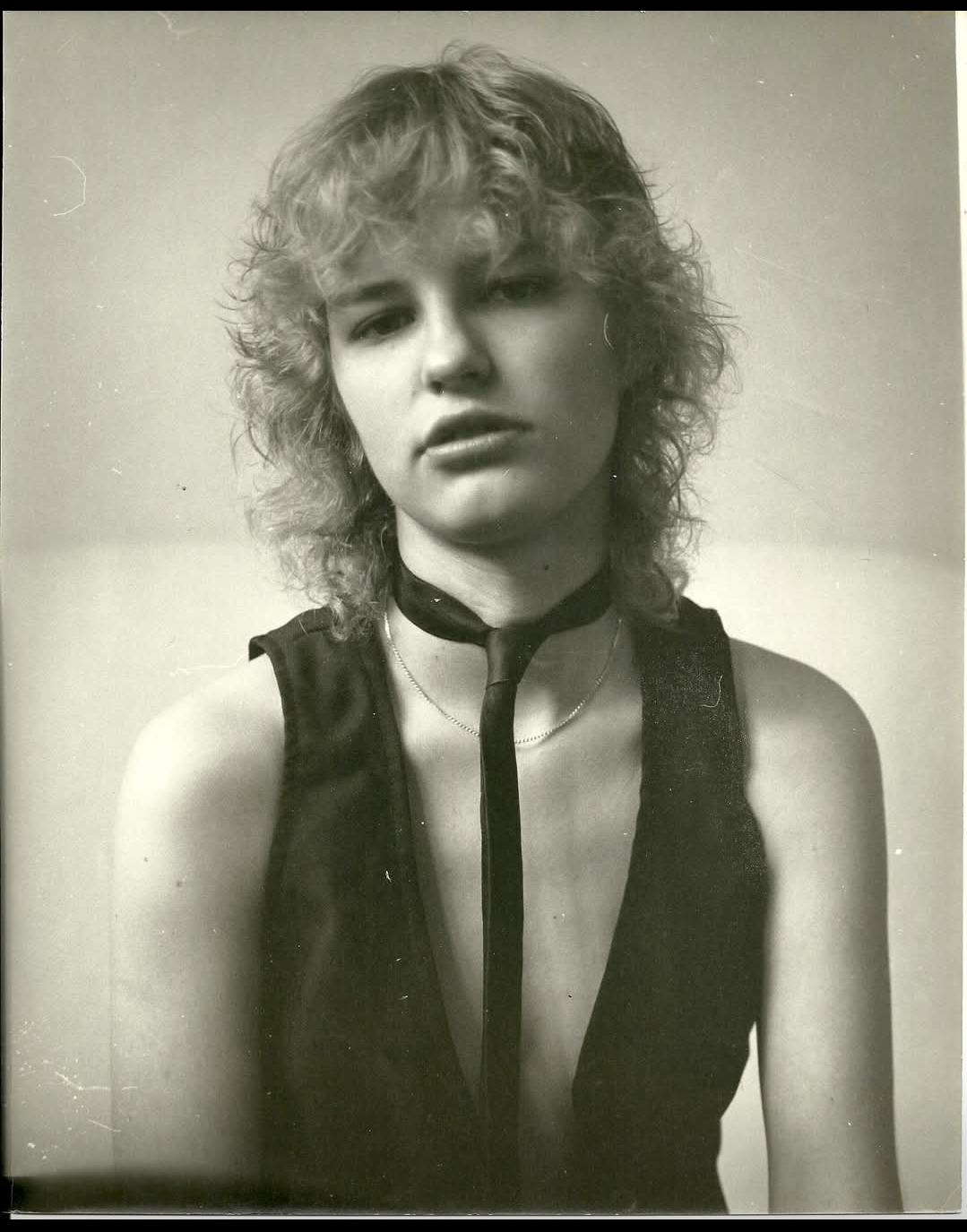 Black and white portrait of a young woman with curly hair wearing a sleeveless top and a choker necklace.