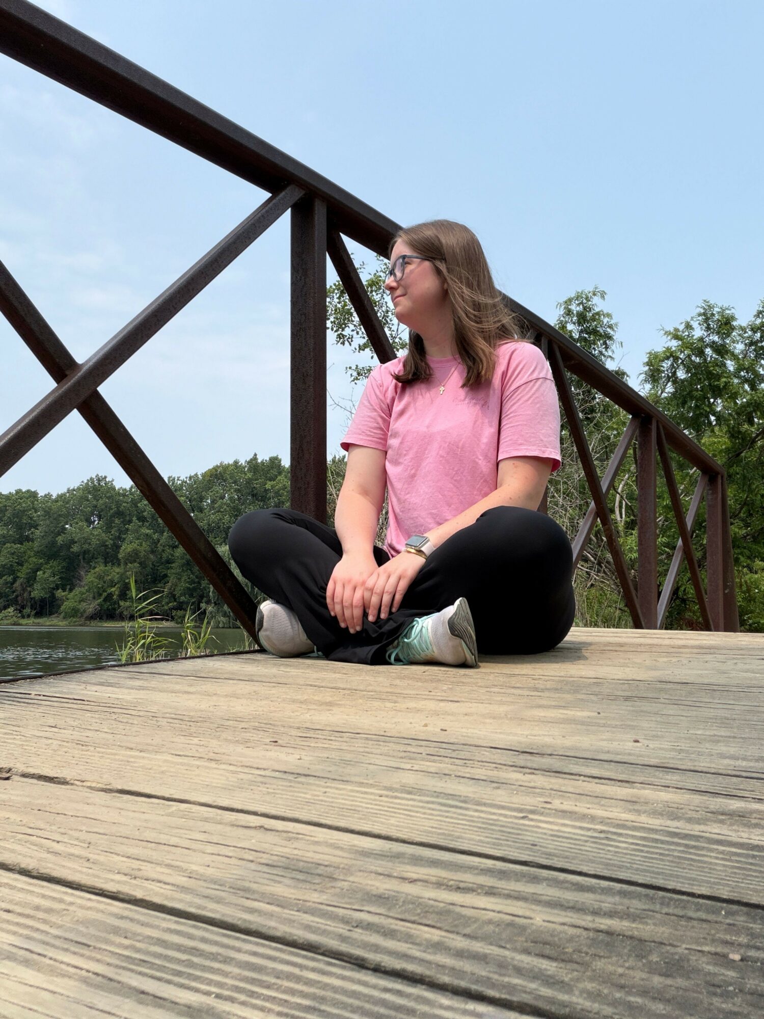 Person sitting on a wooden deck, leaning forward, with trees and sky in the background.