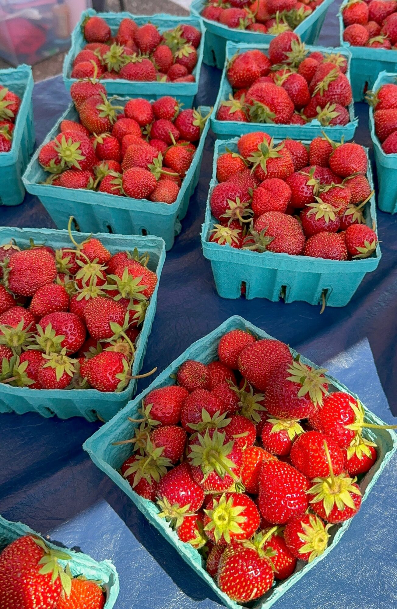 Blue baskets filled with fresh strawberries on a table, some with green leaves attached.
