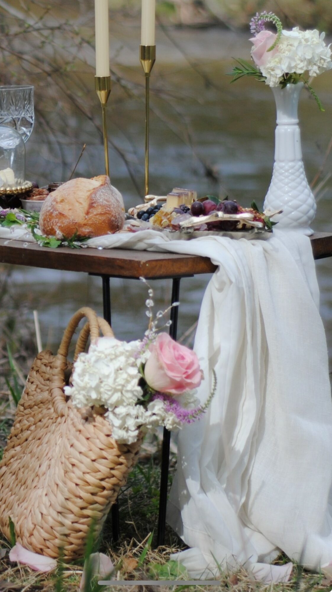 Outdoor table with flowers, cake, and food, decorated with a white cloth, with a basket of flowers nearby.