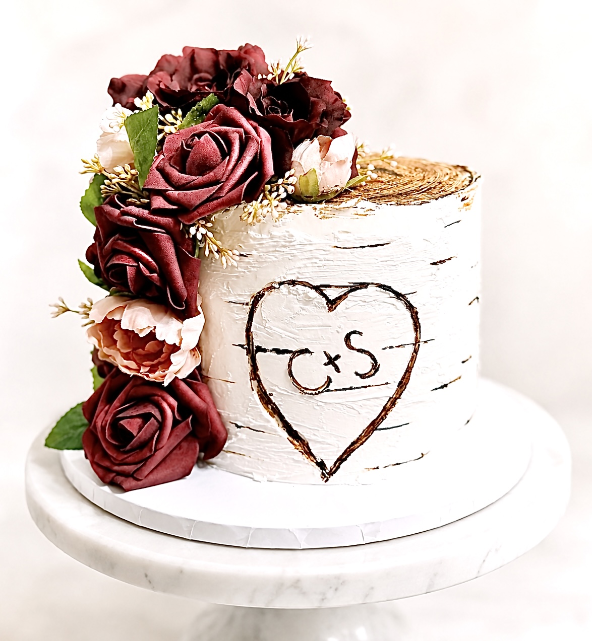 Cake with a heart and initials, decorated with red and pink roses, on a white stand.