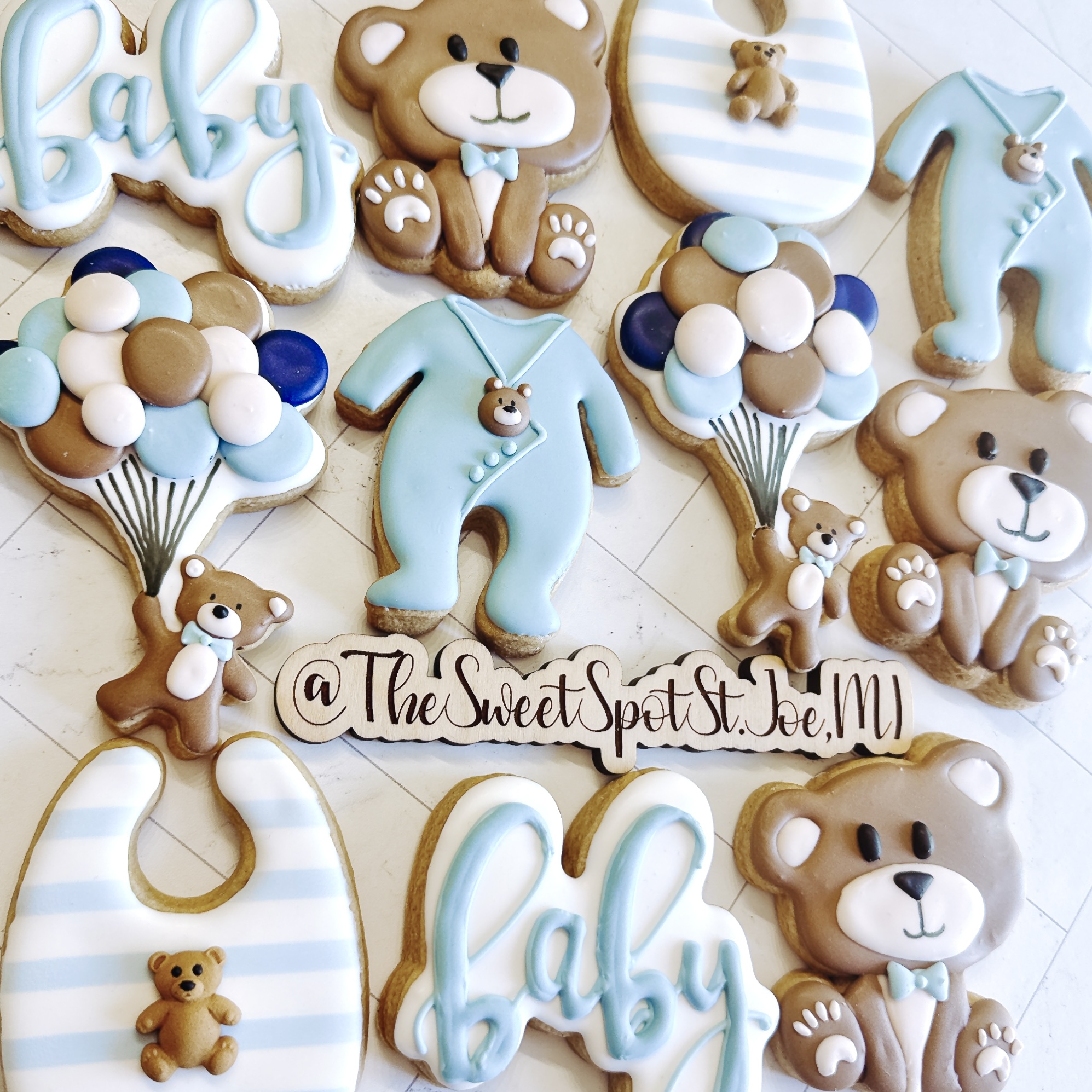 Baby-themed cookies with teddy bears, balloons, and the word 'baby' in pastel colors, arranged on a light surface.