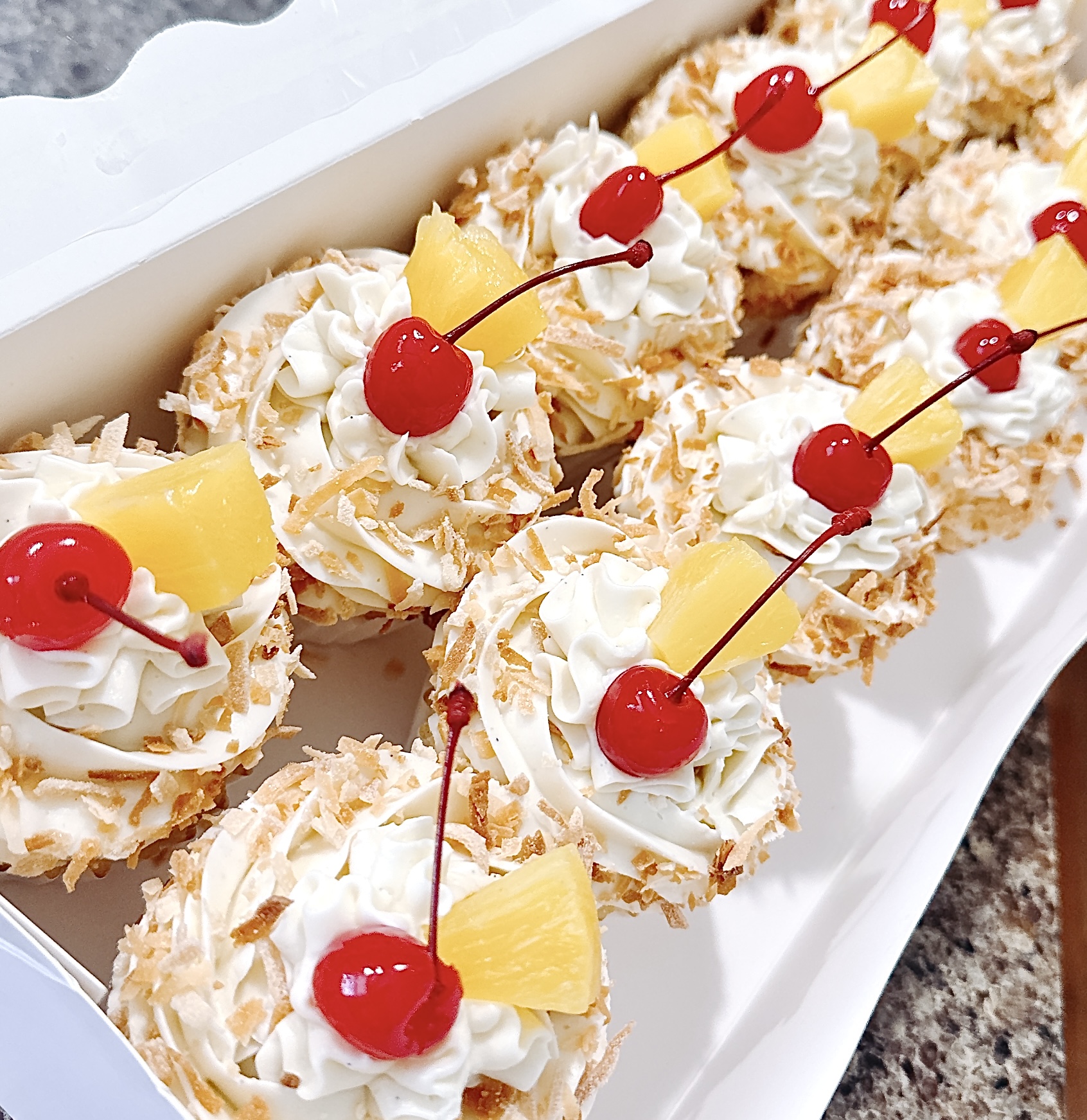 Tray of cream-filled pastries topped with whipped cream, cherries, and pineapple pieces, arranged in a row on a white platter.