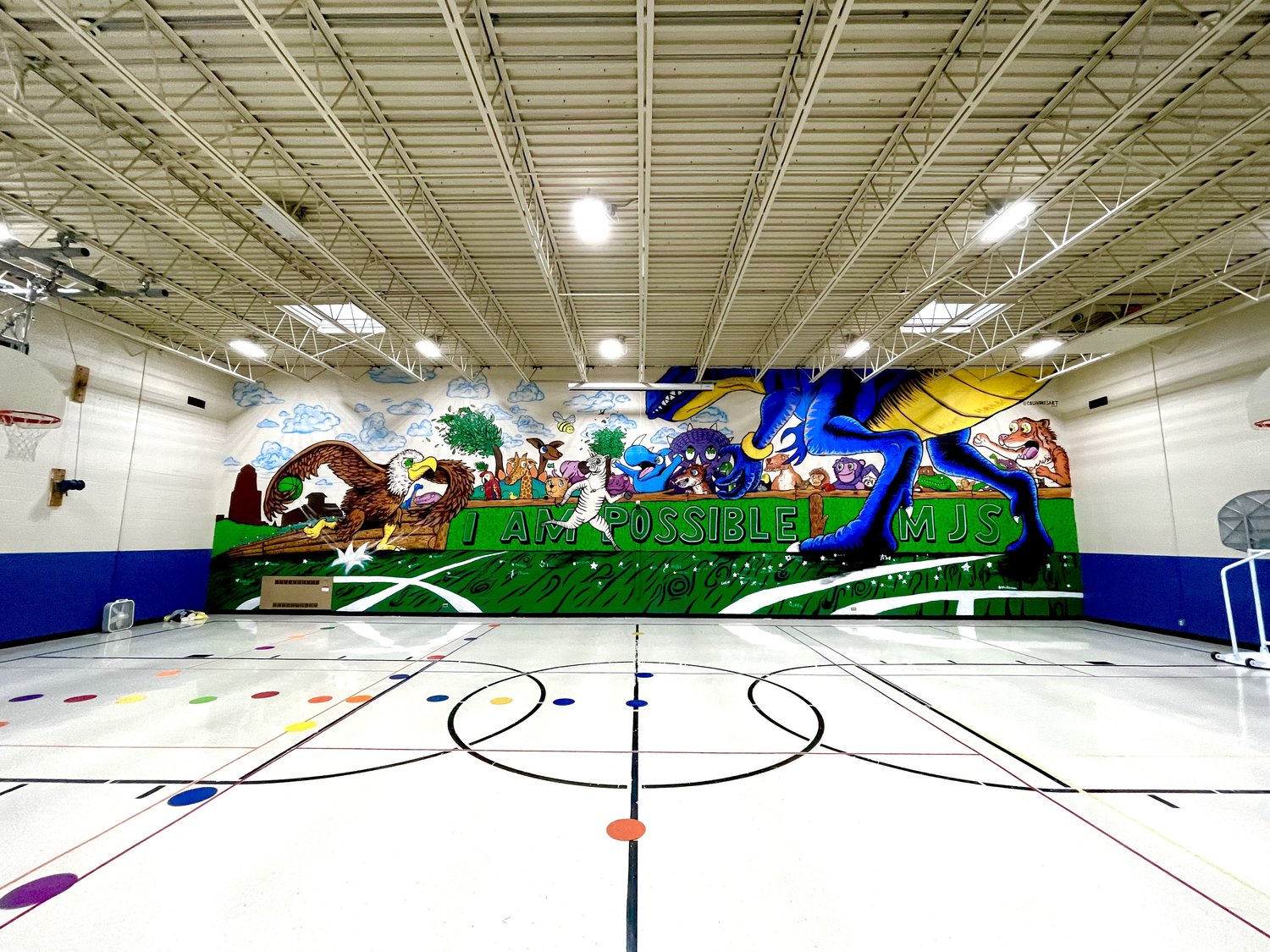 Indoor sports court with a colorful mural on the wall depicting animals and nature scenes, ceiling with lights and structural elements.