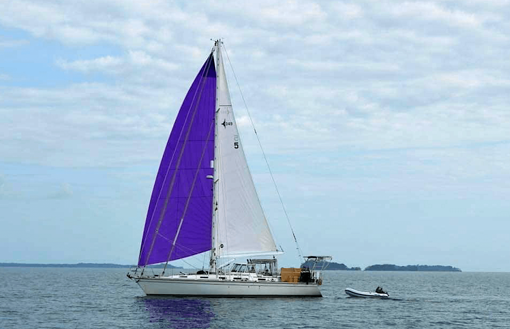 Sailboat with purple and white sails on water, cloudy sky background.
