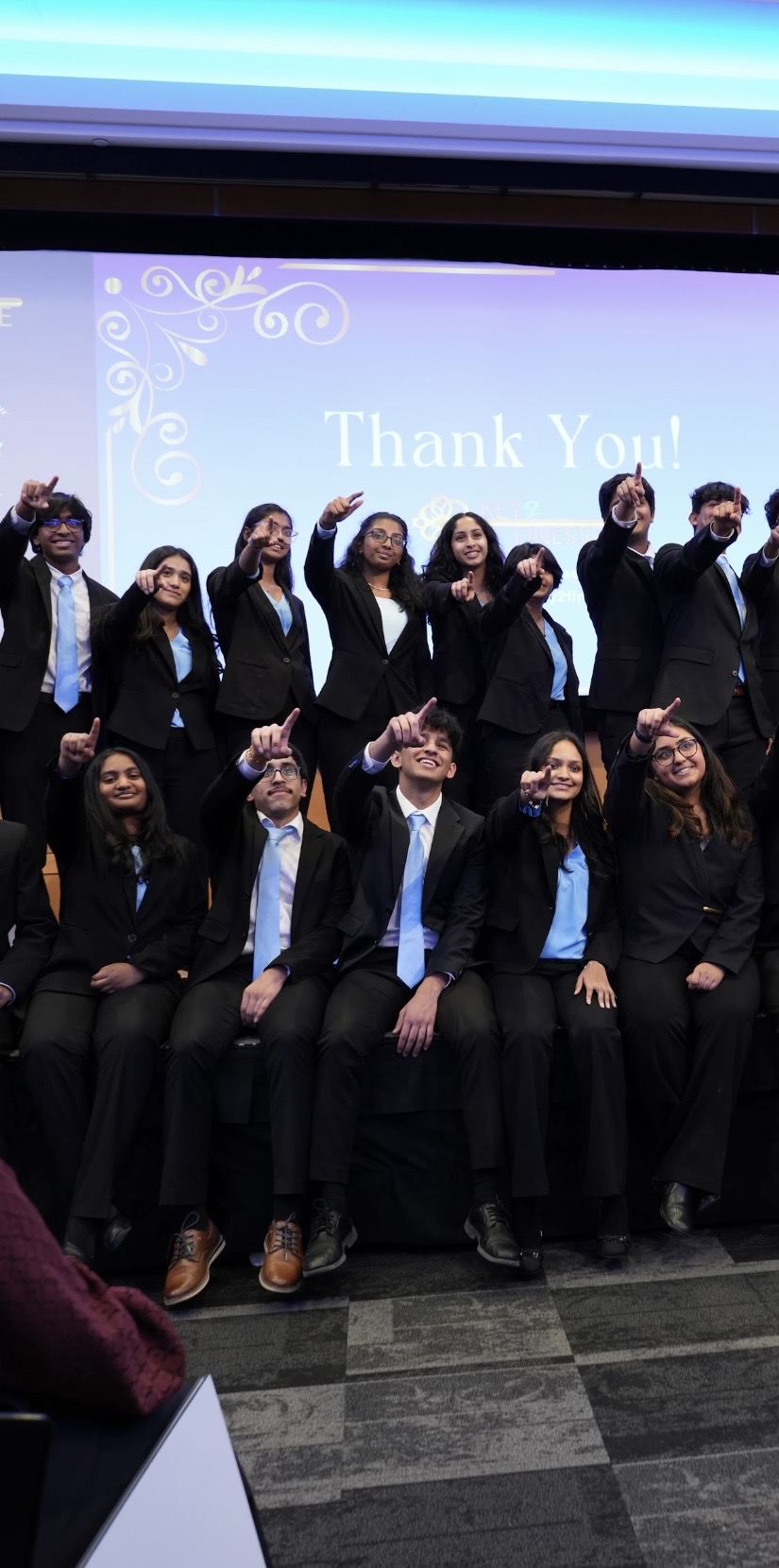 Group of people in formal attire sitting and standing on stage, with a screen behind them displaying 'Thank You!'.