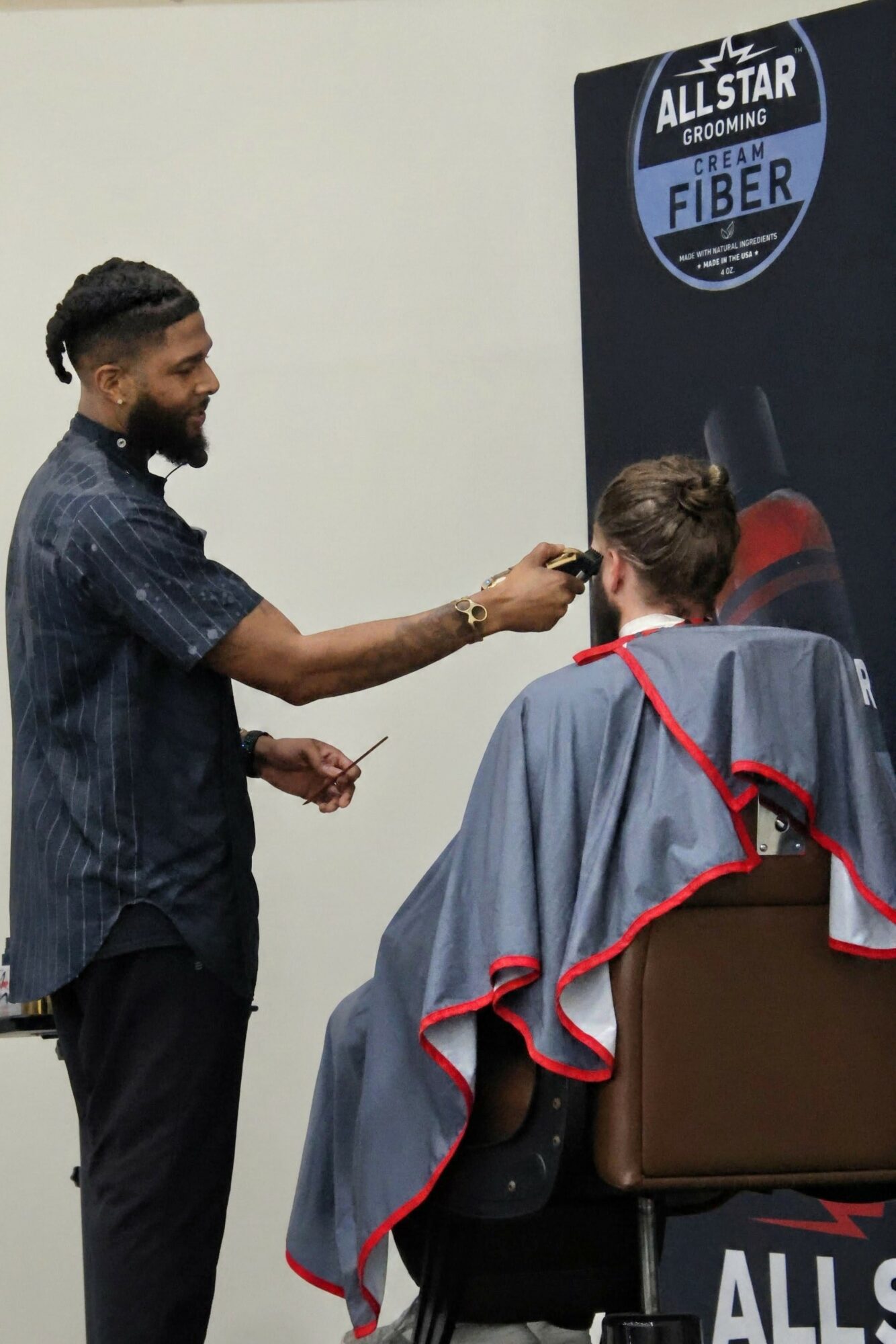 Barber cutting a woman's hair in a salon, with a sign reading 'Allstar Grooming Fiber' in the background.