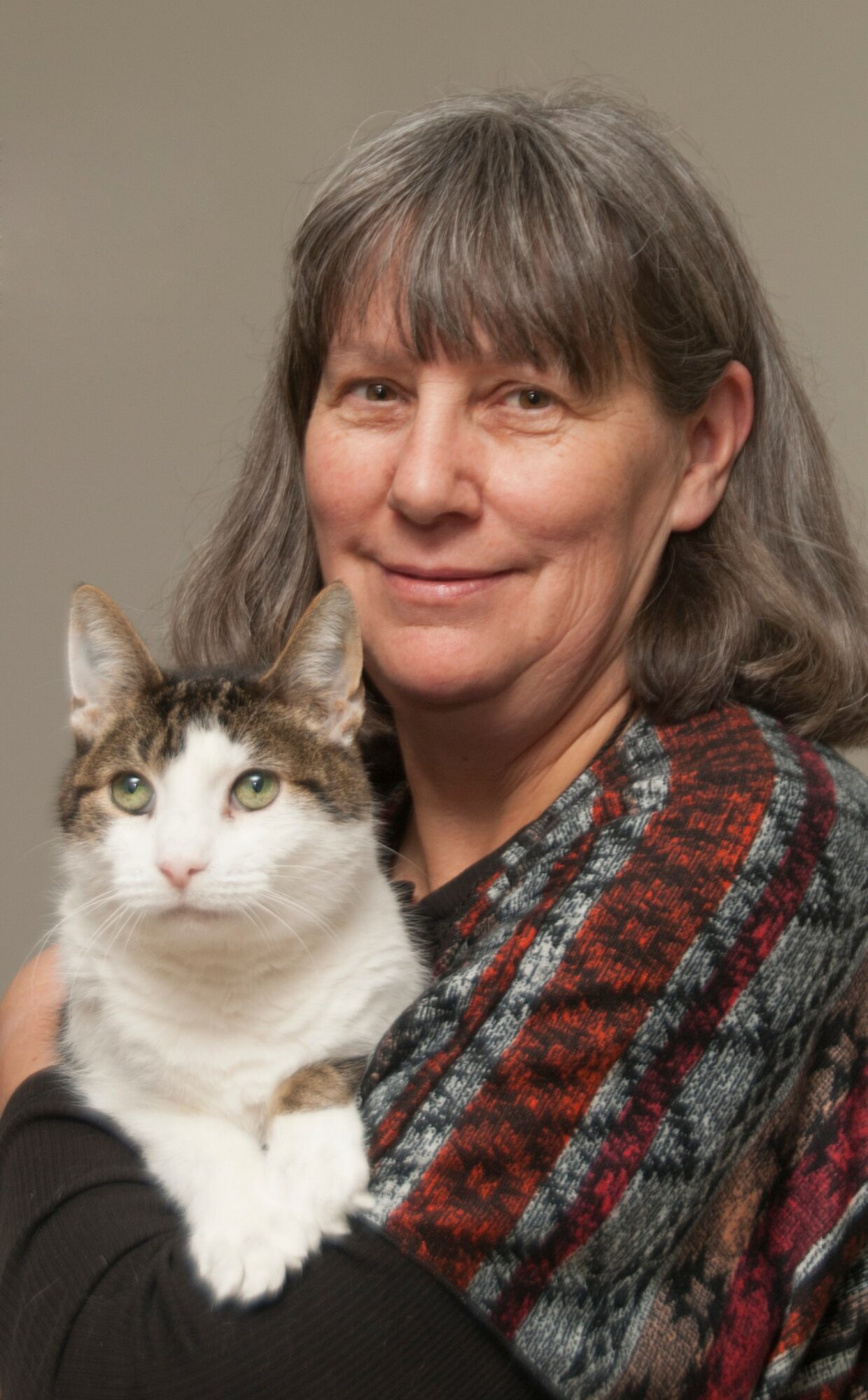 Woman holding a white and gray cat, both looking at the camera, against a plain background.